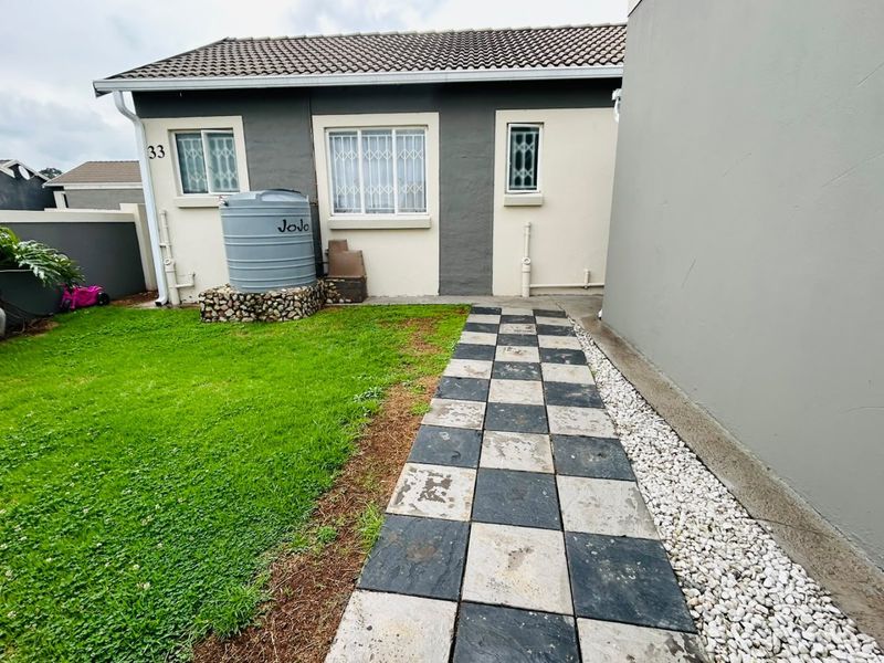 Rear exterior view featuring a small lawn, a checkered tiled walkway, and a water tank installed against the house wall.