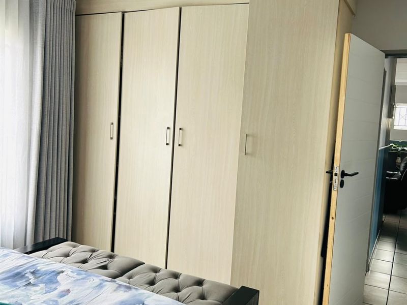 Bedroom featuring light wood-finish built-in cupboards and tiled flooring, with an adjacent hallway visible through the doorway.