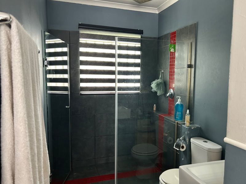 A functional bathroom featuring a glass-enclosed shower, tiled accent wall, toilet, and basin, with dark grey wall finishes.