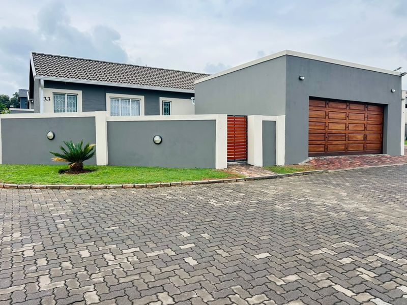 Front elevation of a modern house featuring a paved driveway, a double wooden garage door, and a secure boundary wall with a pedestrian gate.