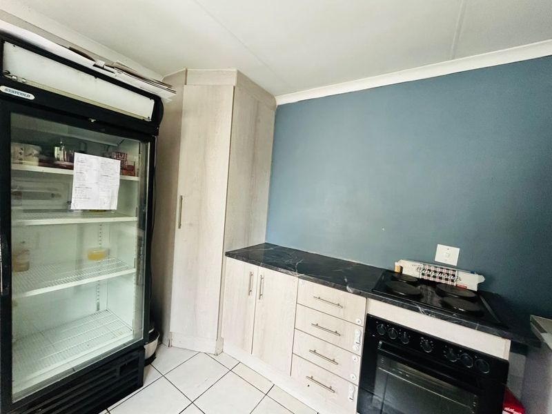 A functional kitchen area featuring light wood-finish cabinetry, dark countertops, a built-in oven with electric hob, and tiled flooring.