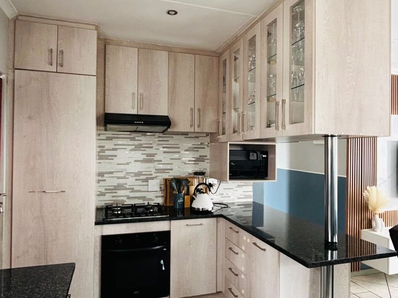 Modern kitchen featuring light wood cabinetry, granite countertops, a gas hob, built-in oven, and a convenient breakfast bar with tiled flooring.