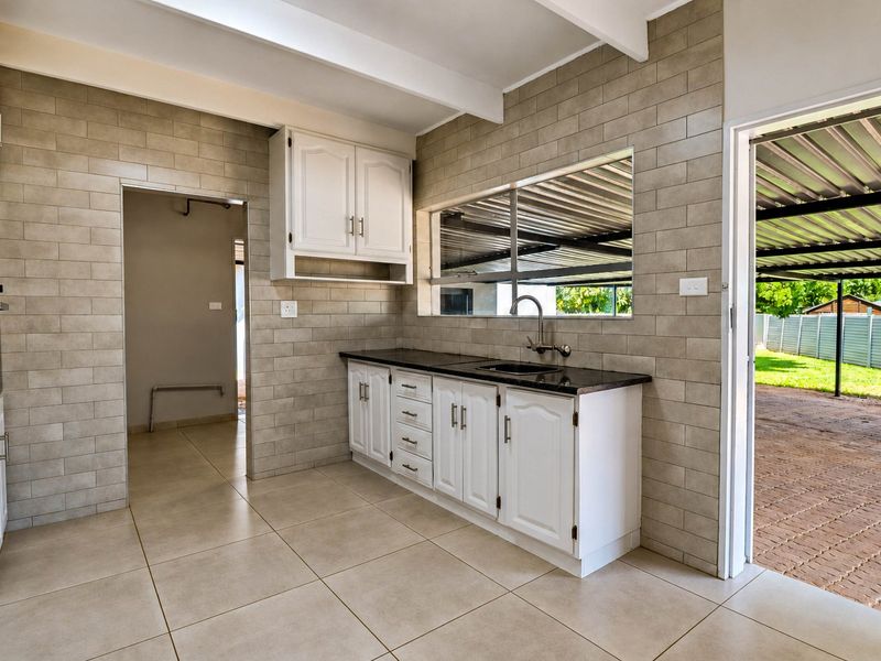 A clean, functional kitchen featuring white cabinetry, granite countertops, tiled backsplash, and exposed ceiling beams, with direct access to an outdoor patio area.
