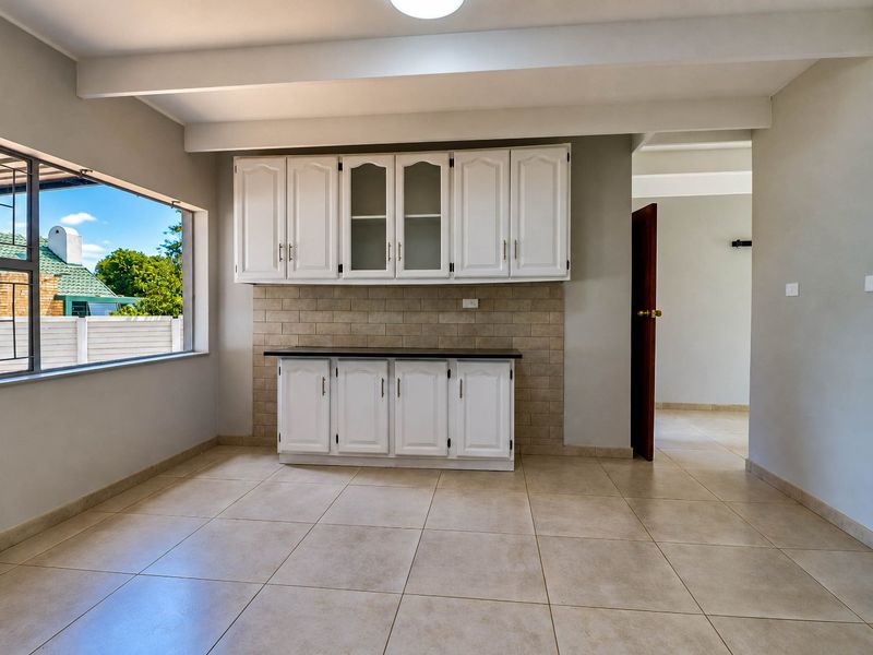 A bright, empty kitchen area featuring white built-in cabinetry, a neutral tiled backsplash, and large floor tiles with an exposed ceiling beam.