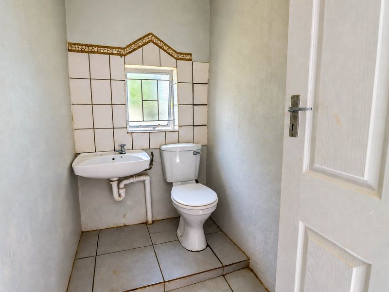 A compact guest bathroom featuring a wall-mounted basin, toilet, and tiled splashback, requiring cosmetic updates to improve its overall condition.