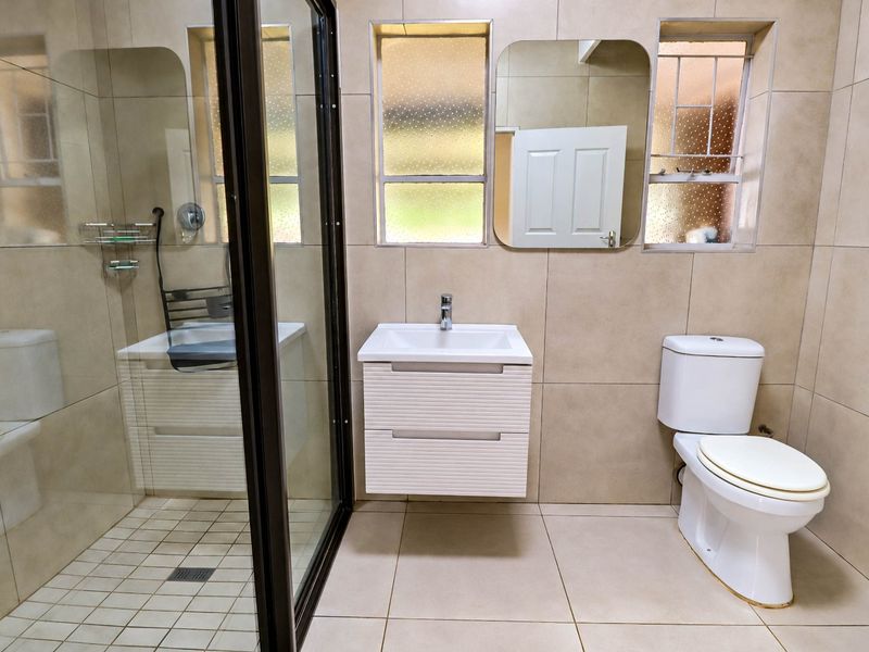 A modern bathroom featuring a glass-enclosed shower, a wall-mounted vanity with basin, and a toilet, finished with neutral floor-to-ceiling wall tiles.