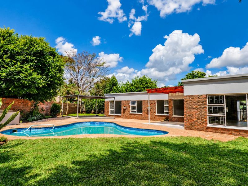 Rear view of the property featuring a swimming pool, paved patio area, and a brick facade with large windows.