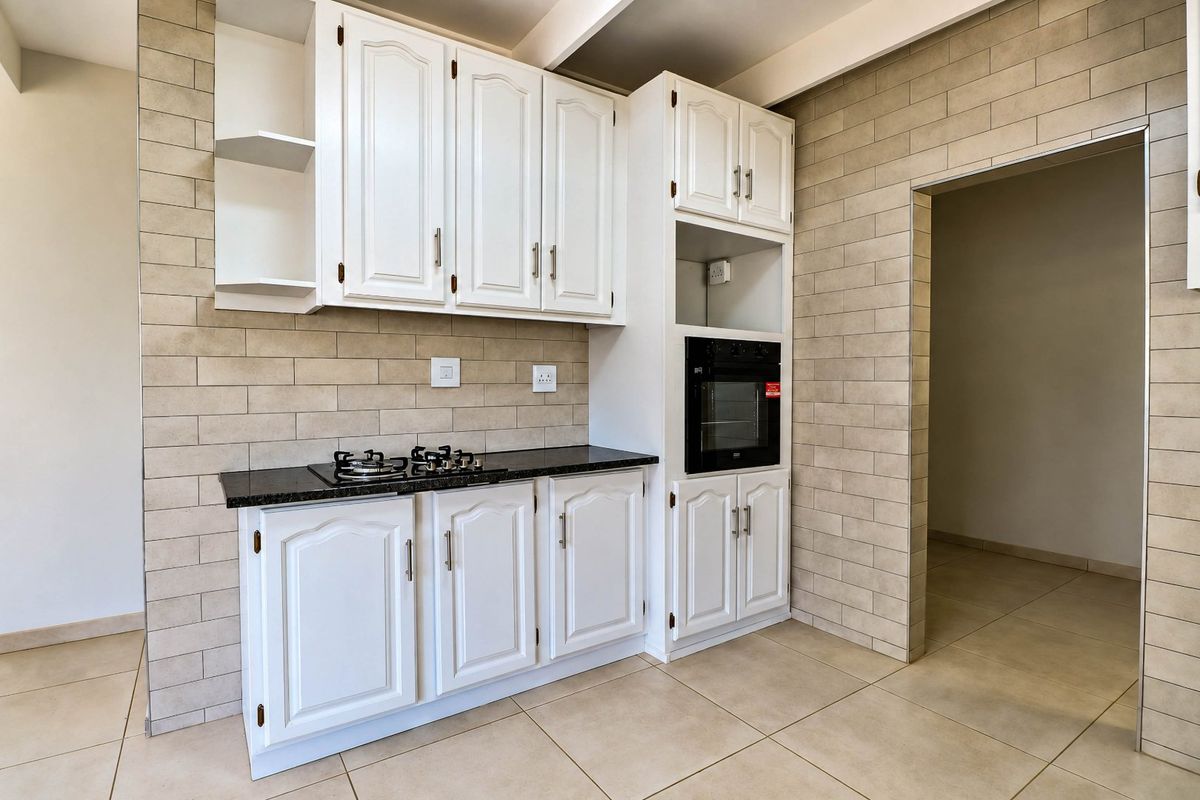A clean, functional kitchen featuring white cabinetry, black granite countertops, a built-in oven, and a gas hob with neutral tiled finishes.