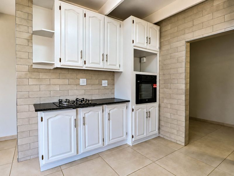 A clean, functional kitchen featuring white cabinetry, black granite countertops, a built-in oven, and a gas hob with neutral tiled finishes.