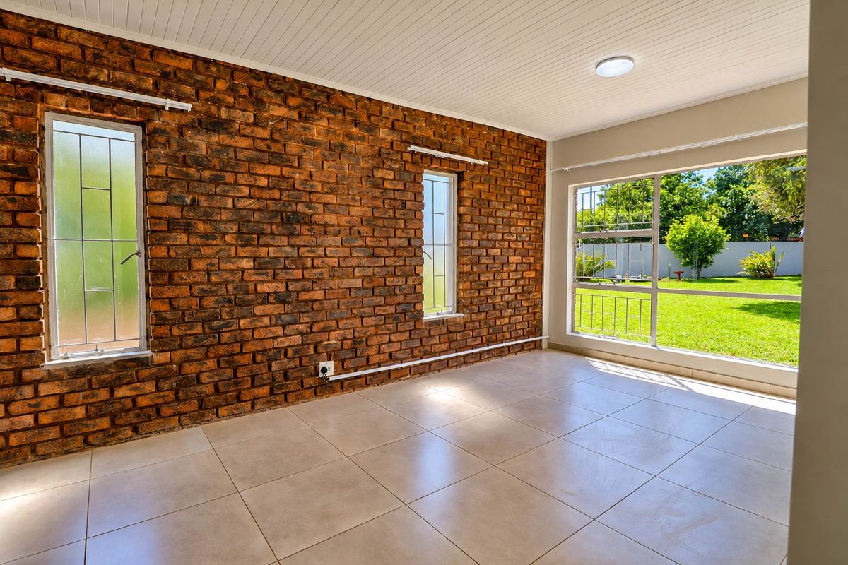 Bright and spacious living area featuring an exposed brick wall, neutral tiled flooring, and large windows overlooking the garden.