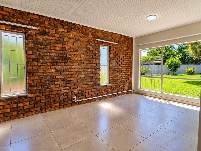 Bright and spacious living area featuring an exposed brick wall, neutral tiled flooring, and large windows overlooking the garden.