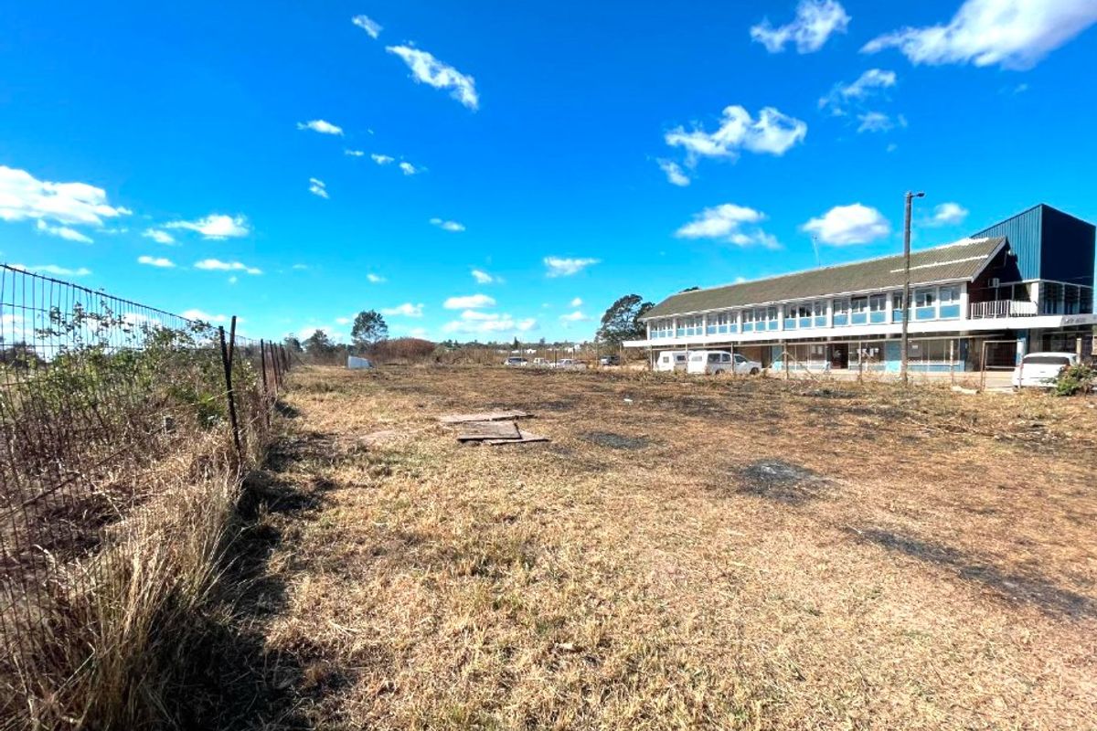 A view of the rear exterior grounds and commercial building structure, featuring a chain-link perimeter fence and open land area.