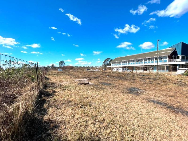A view of the rear exterior grounds and commercial building structure, featuring a chain-link perimeter fence and open land area.