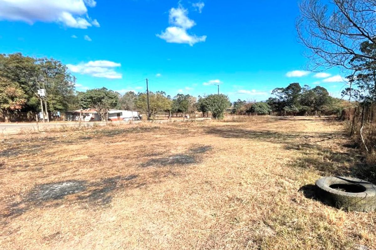 A large, undeveloped commercial plot of land featuring dry grass, perimeter fencing, and utility infrastructure, suitable for future development.