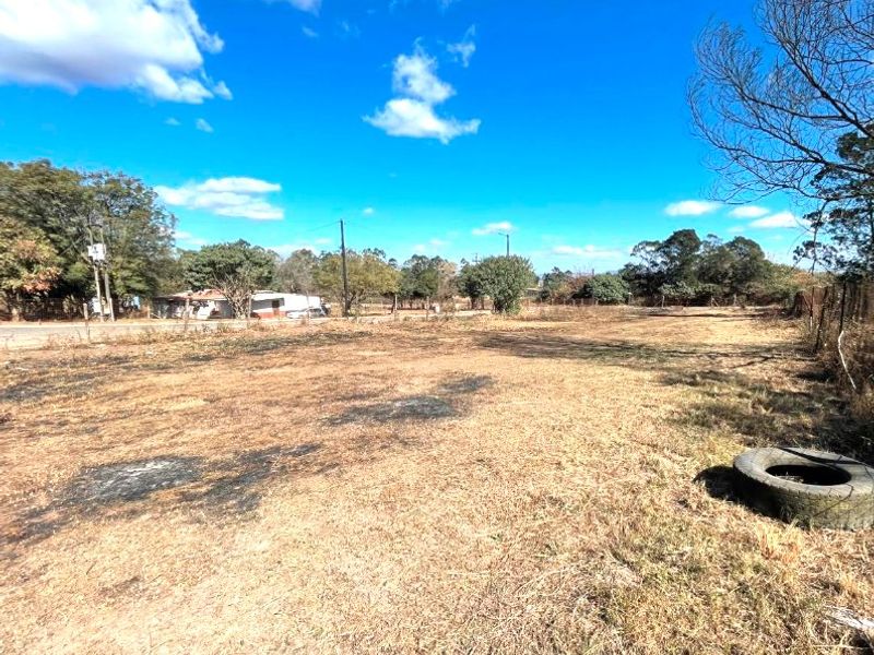 A large, undeveloped commercial plot of land featuring dry grass, perimeter fencing, and utility infrastructure, suitable for future development.
