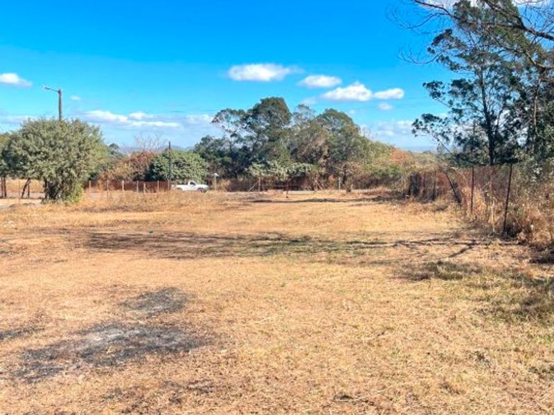 An expansive, undeveloped plot of land featuring dry grass, perimeter wire fencing, and mature trees in the background.