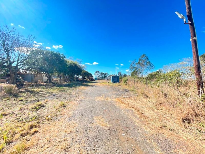 An expansive outdoor commercial plot featuring a gravel access path, utility infrastructure, and perimeter fencing, surrounded by natural vegetation.