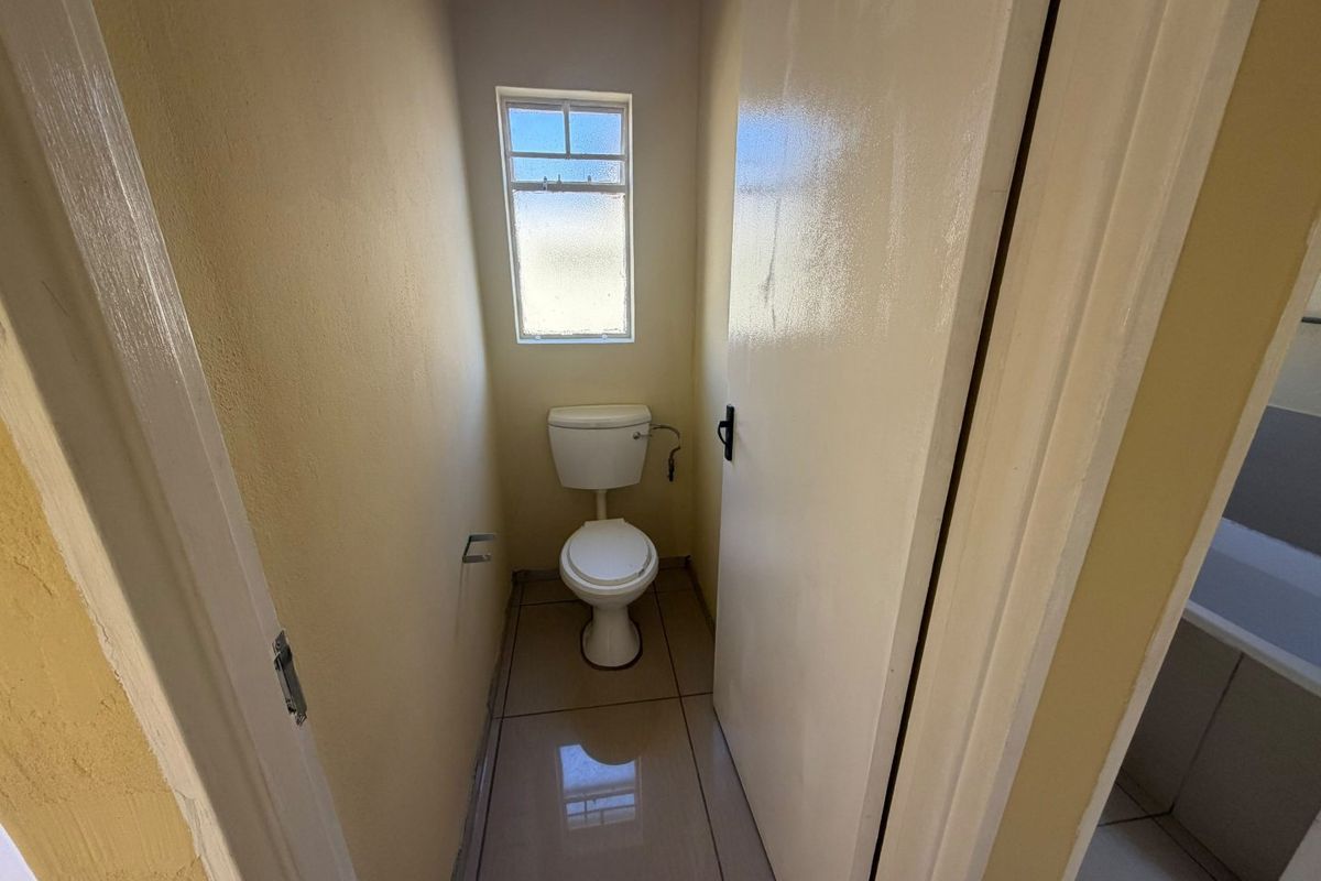 A compact, functional guest toilet featuring tiled flooring and a window for natural light.
