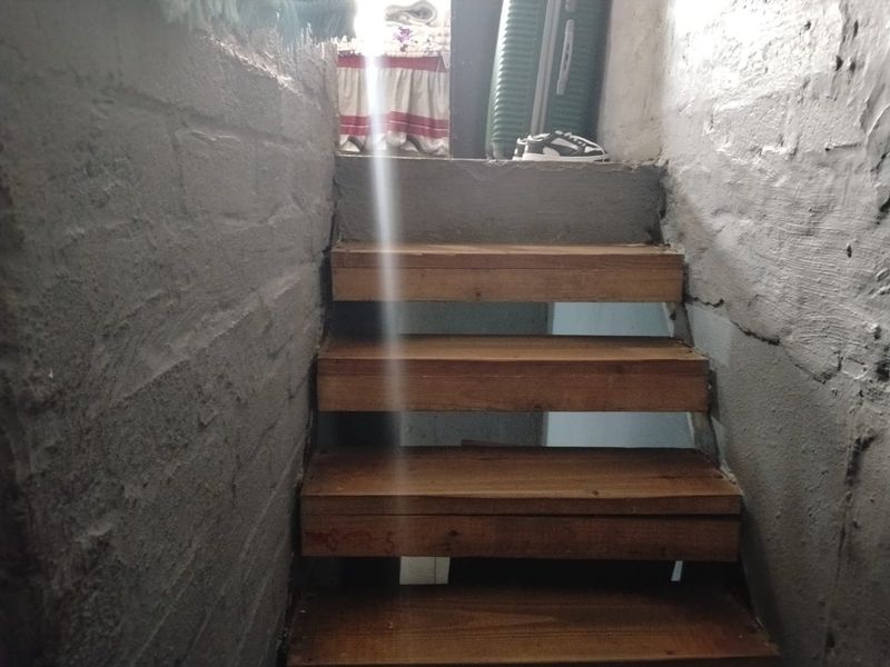 A narrow staircase featuring wooden treads set between unfinished masonry walls, leading to an upper level.