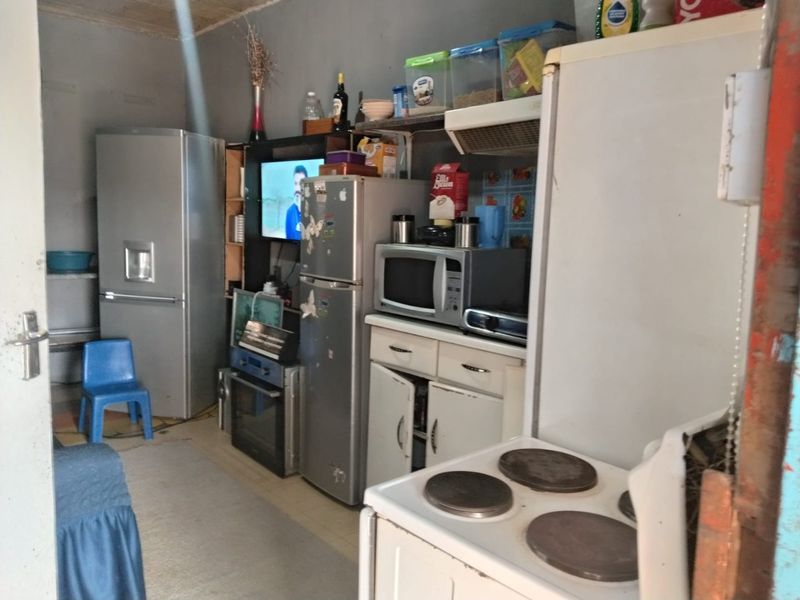 A compact kitchen area featuring basic cabinetry, an electric stove, and an extractor fan, requiring cosmetic updates to improve functionality and aesthetic appeal.