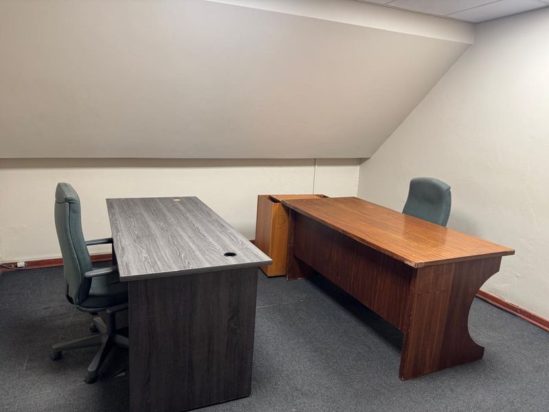 A functional office space featuring a sloped ceiling and carpeted flooring, suitable for a professional work environment.