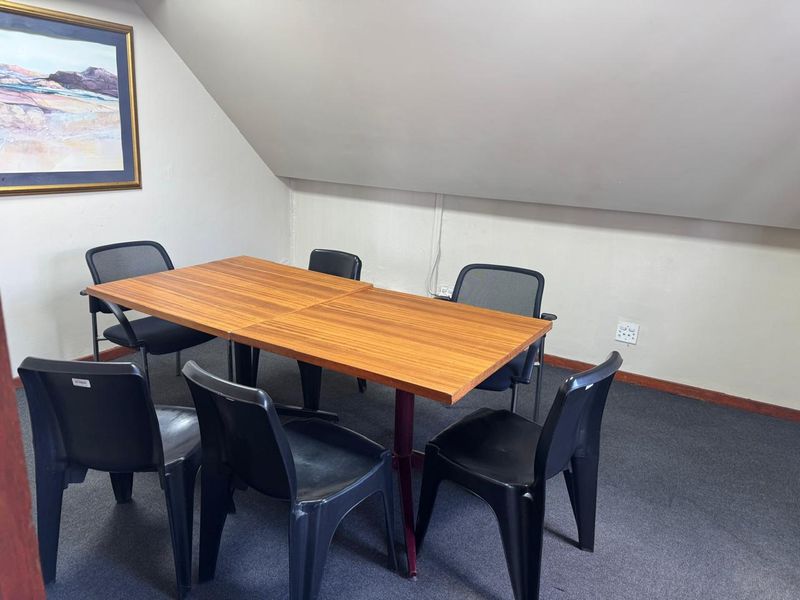 A functional office space featuring a sloped ceiling, carpeted flooring, and standard electrical infrastructure, suitable for a meeting or workspace area.