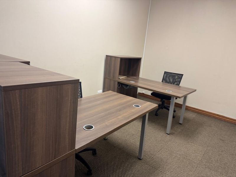 A functional office space featuring neutral wall finishes and patterned carpet flooring, suitable for a professional work environment.