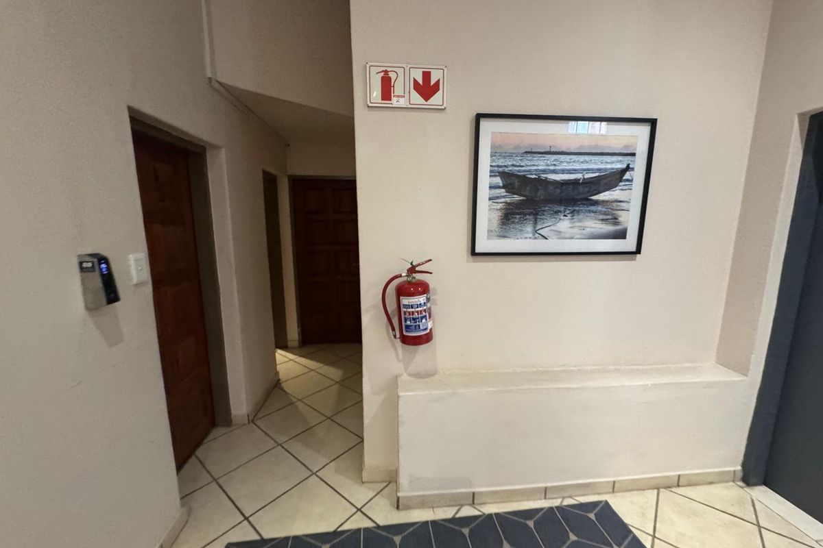 A clean commercial hallway featuring tiled flooring, wooden doors, and essential fire safety equipment including a wall-mounted fire extinguisher and signage.