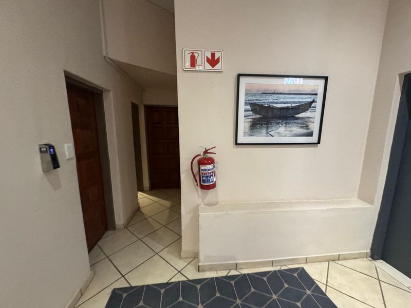 A clean commercial hallway featuring tiled flooring, wooden doors, and essential fire safety equipment including a wall-mounted fire extinguisher and signage.