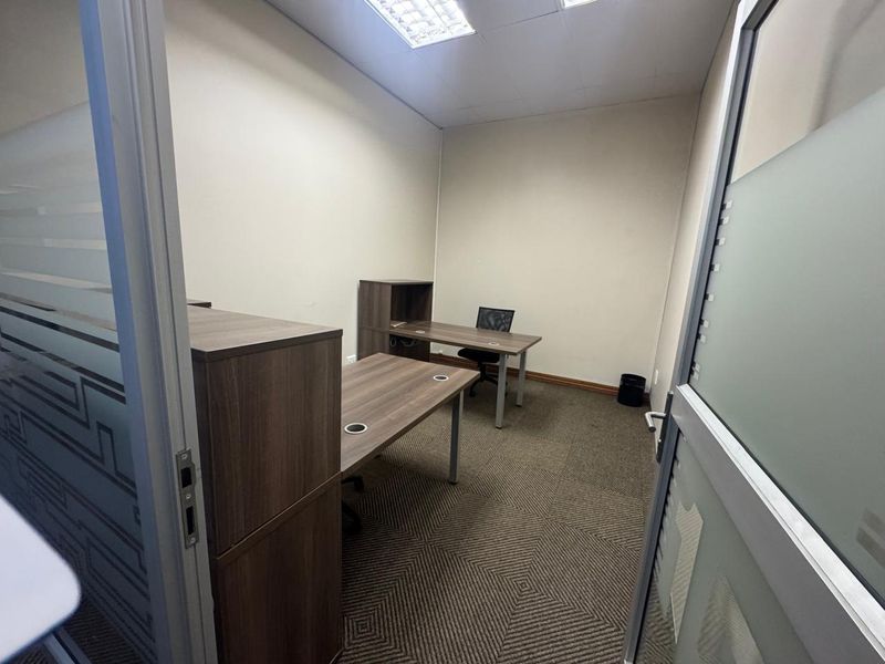 A functional office space featuring carpeted flooring, a suspended ceiling with recessed lighting, and a modern frosted glass entry door.