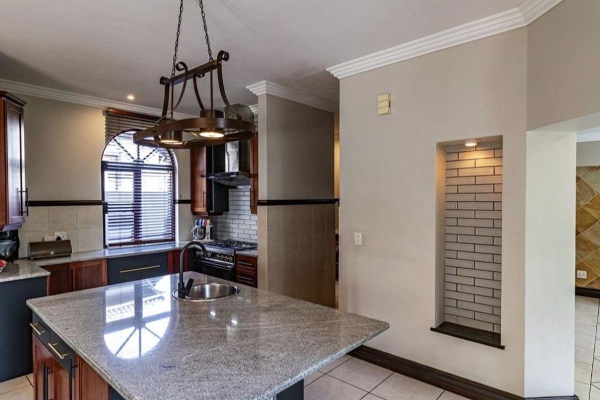 Modern kitchen featuring a large granite-topped island with an undermount sink, built-in gas hob, extractor fan, and a decorative recessed wall niche.