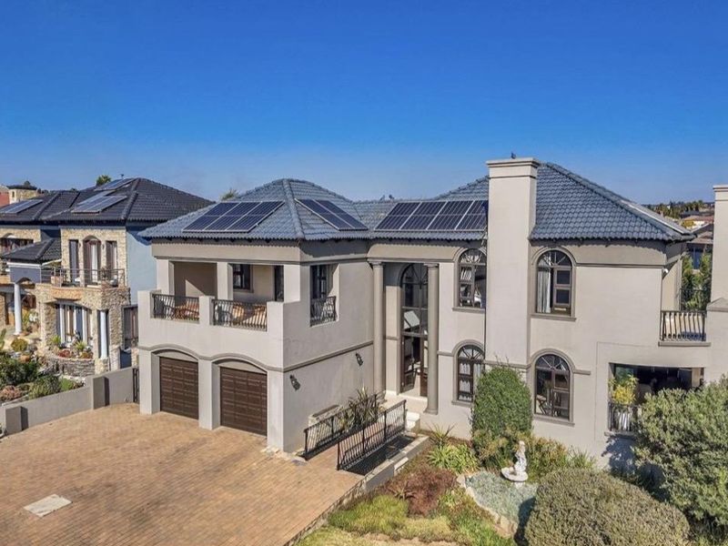 An elevated view of a modern two-story residential property featuring a paved driveway, double garage, solar panels, and a balcony.