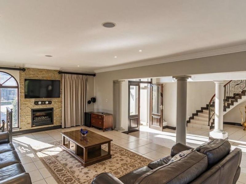 Spacious open-plan living area featuring a stone-clad fireplace, tiled flooring, structural columns, and an elegant staircase with wrought iron detailing.