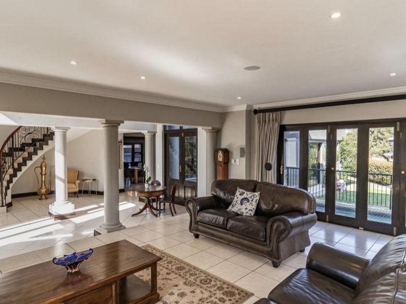 Spacious open-plan living area featuring tiled floors, recessed lighting, elegant structural columns, and direct access to the garden through large french doors.