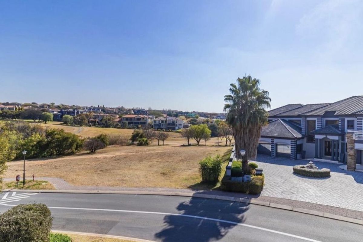 Aerial view of a modern luxury residence featuring a paved driveway, multi-car garage, and stone-clad facade, situated in a scenic estate setting.