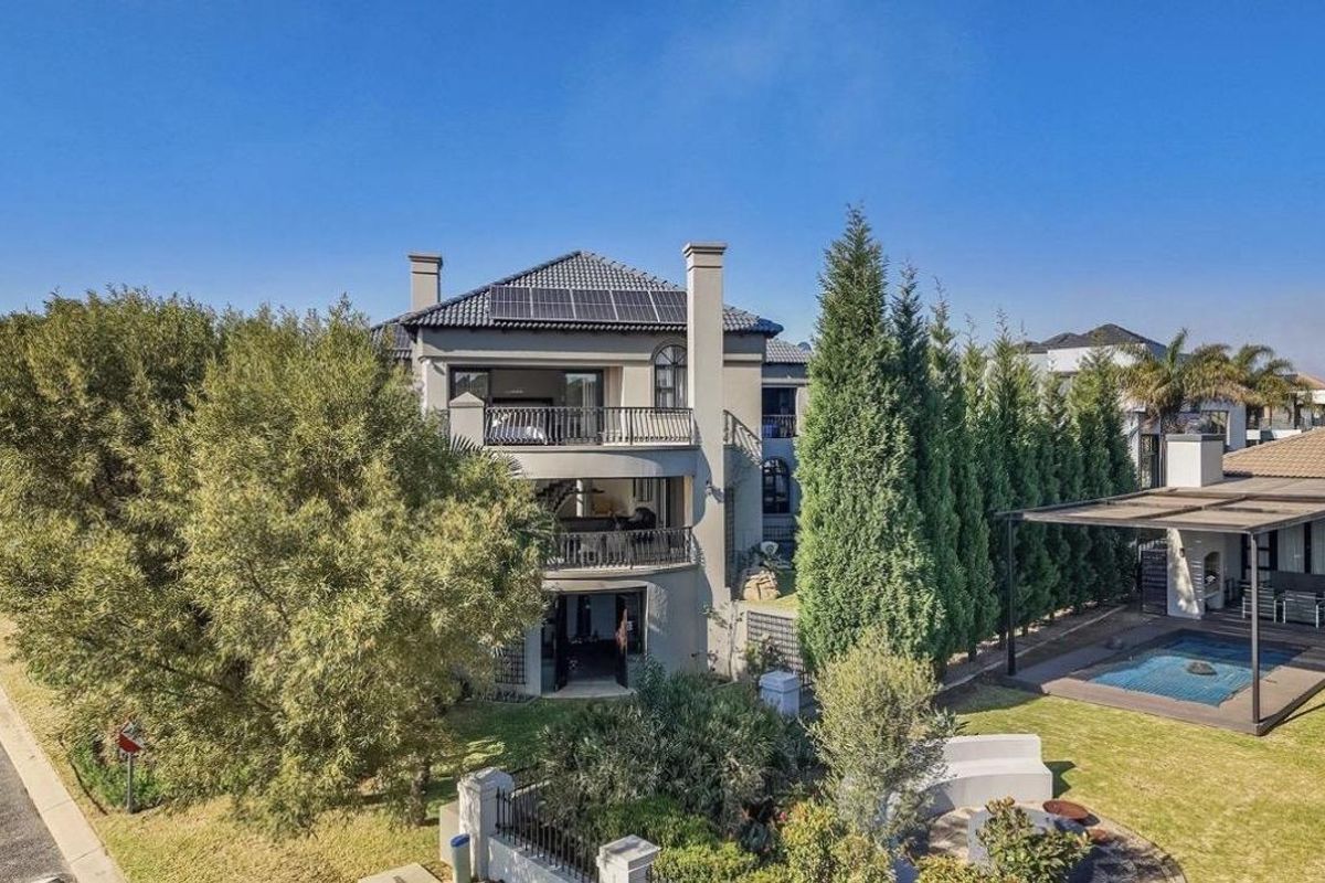 Rear view of a multi-story residential property featuring stacked balconies, solar panels, a swimming pool, and a covered patio area within a landscaped garden.