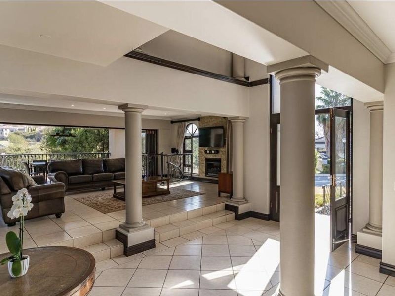 Spacious open-plan living area featuring tiled floors, decorative columns, a fireplace, and large sliding doors opening to an outdoor balcony.