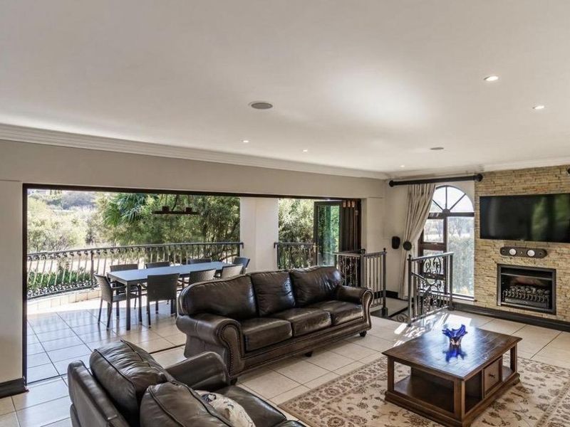 Spacious open-plan living area featuring a stone-clad fireplace, recessed lighting, and large stacking doors opening onto a tiled balcony with scenic views.