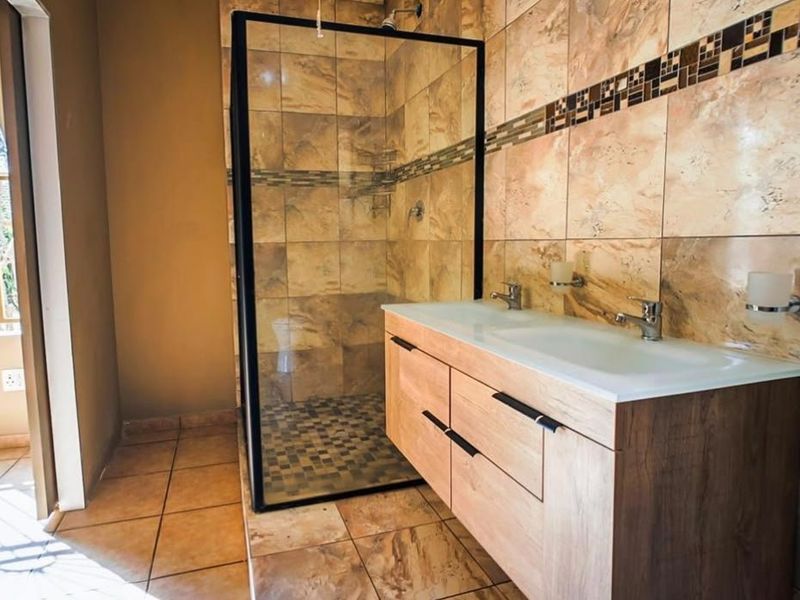 A modern bathroom featuring a walk-in shower with a black frame, a double vanity unit, and neutral-toned tiled finishes throughout.