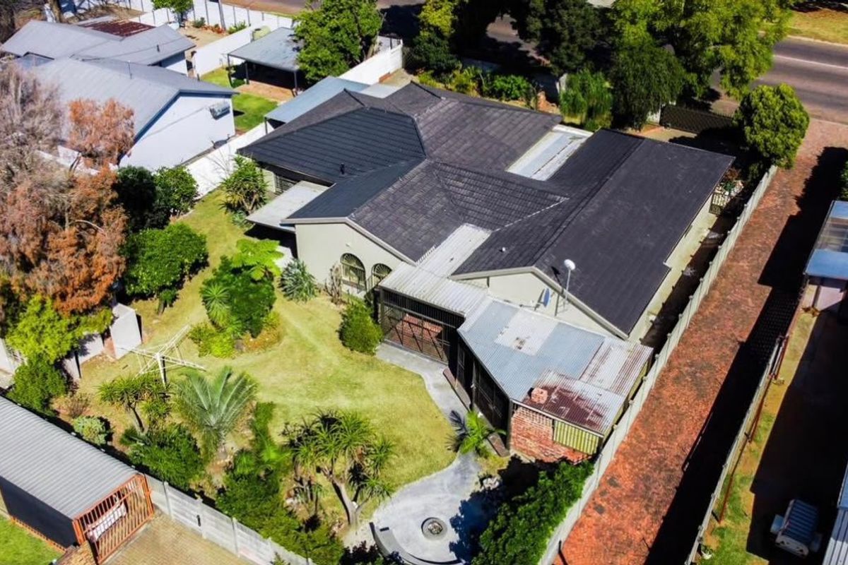 Aerial view of the property showcasing the house layout, tiled roof, surrounding garden, and driveway access within the residential neighborhood.