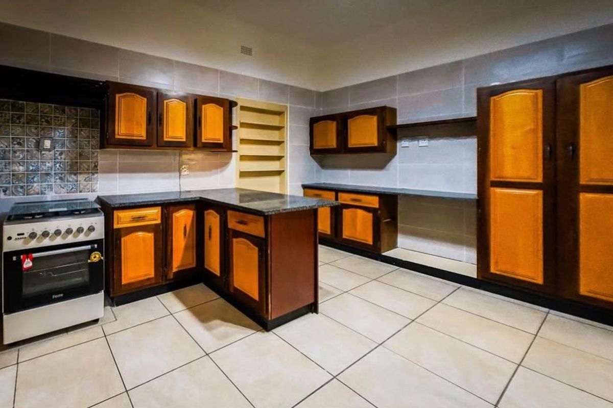 A spacious kitchen featuring built-in wooden cabinetry, granite countertops, tiled walls, and a freestanding stove, offering a functional layout with ample storage space.