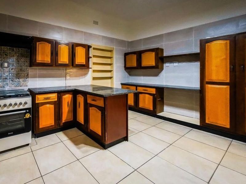 A spacious kitchen featuring built-in wooden cabinetry, granite countertops, tiled walls, and a freestanding stove, offering a functional layout with ample storage space.