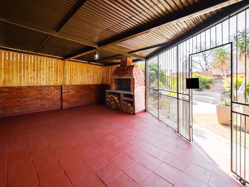 Covered outdoor patio featuring a built-in brick braai, tiled flooring, and secure metal gate access to the garden area.