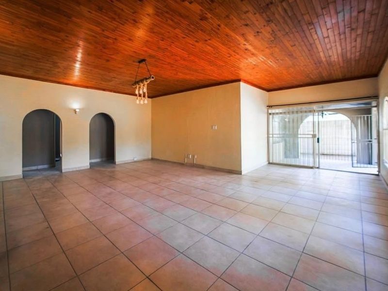 Spacious living area featuring a timber tongue and groove ceiling, ceramic tiled flooring, and arched doorways leading to adjacent rooms.