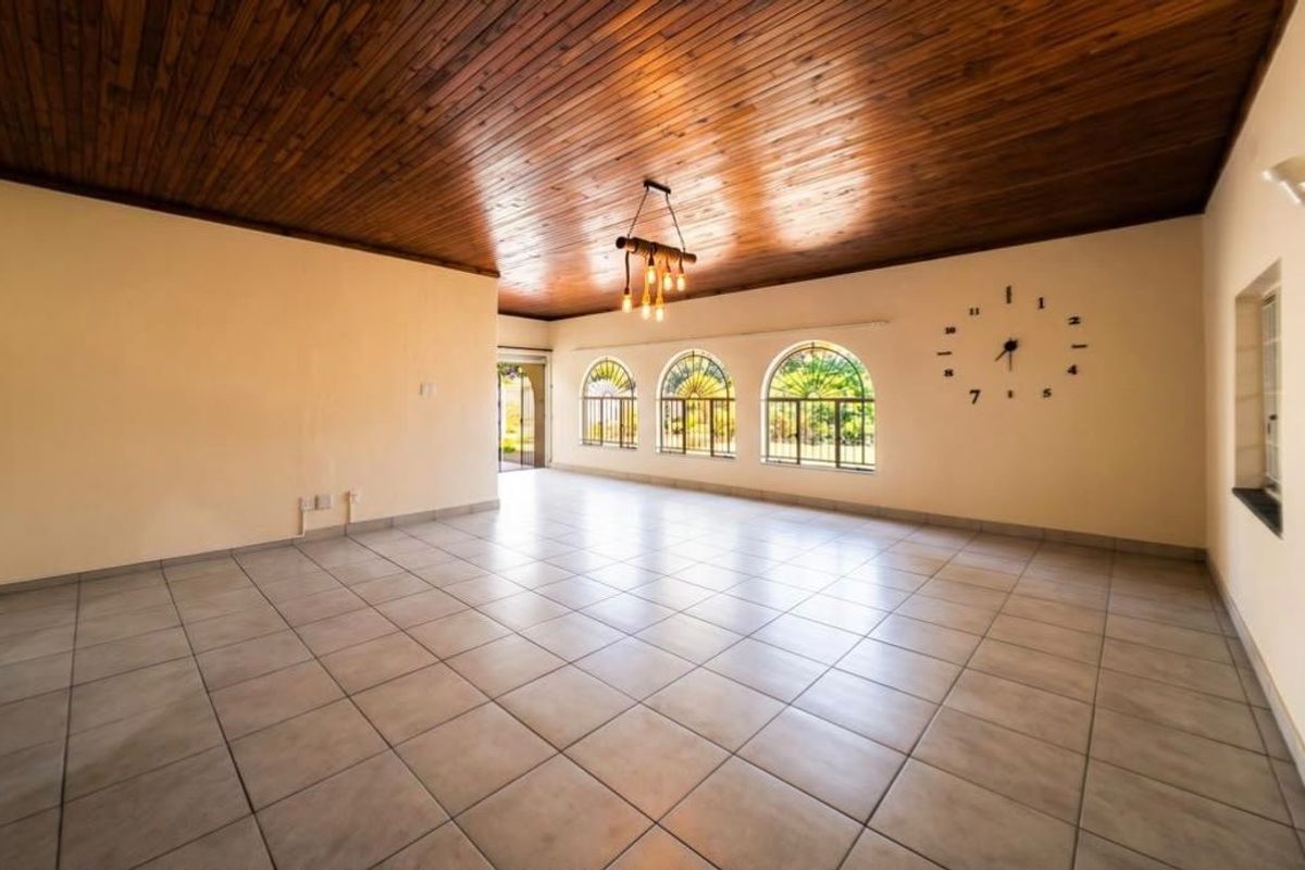 Spacious living area featuring a warm timber tongue and groove ceiling, large arched windows with security bars, and neutral ceramic floor tiles.