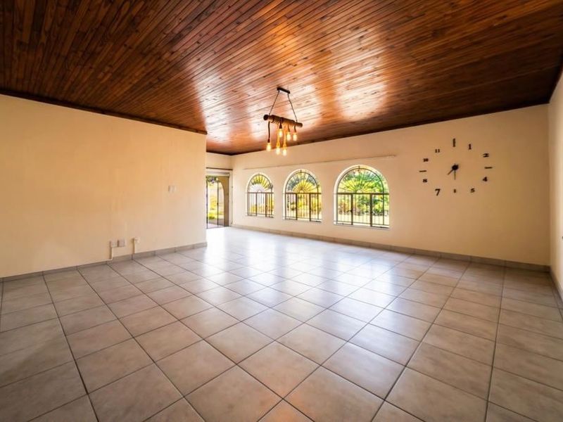 Spacious living area featuring a warm timber tongue and groove ceiling, large arched windows with security bars, and neutral ceramic floor tiles.