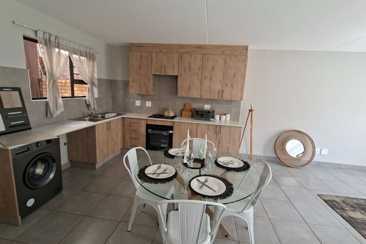 Open-plan kitchen and dining area featuring modern wood-look cabinetry, integrated appliances, tiled flooring, and a neutral color palette.