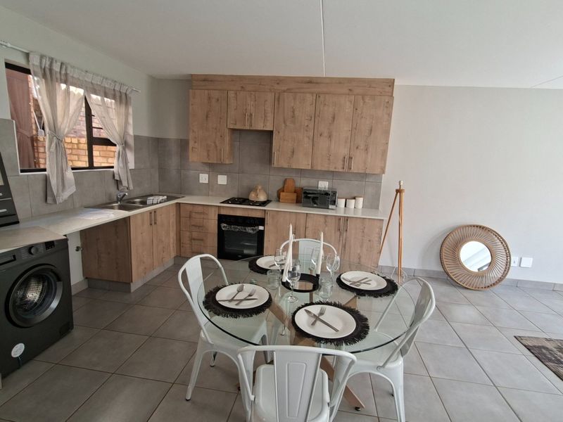 Open-plan kitchen and dining area featuring modern wood-look cabinetry, integrated appliances, tiled flooring, and a neutral color palette.