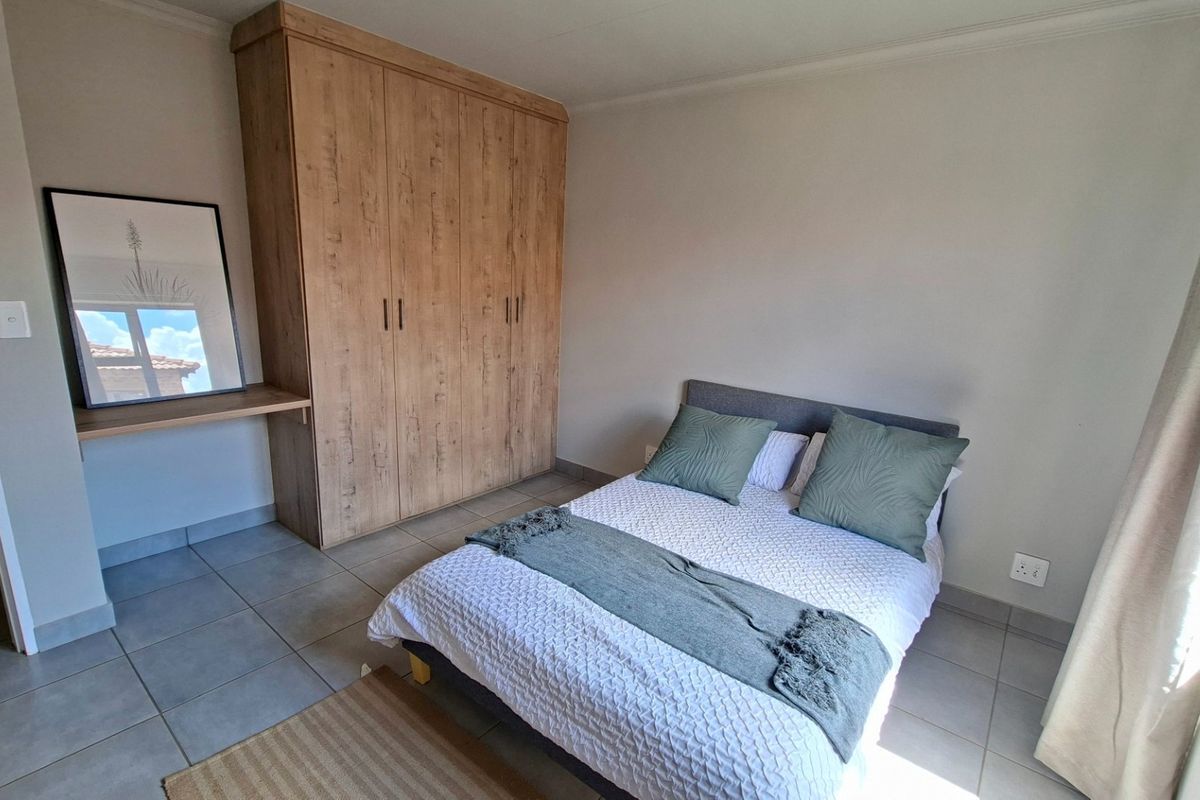 A well-maintained bedroom featuring neutral tiled flooring, a modern built-in wardrobe with an integrated desk area, and ample natural light.
