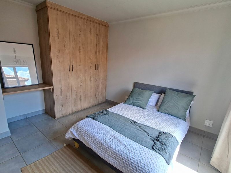 A well-maintained bedroom featuring neutral tiled flooring, a modern built-in wardrobe with an integrated desk area, and ample natural light.